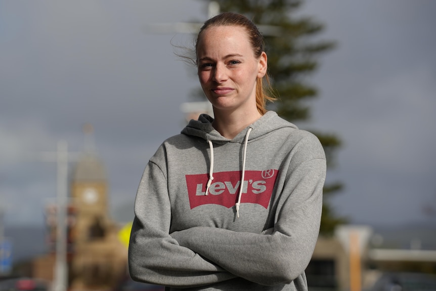 A woman wearing grey jumper with arms crossed.