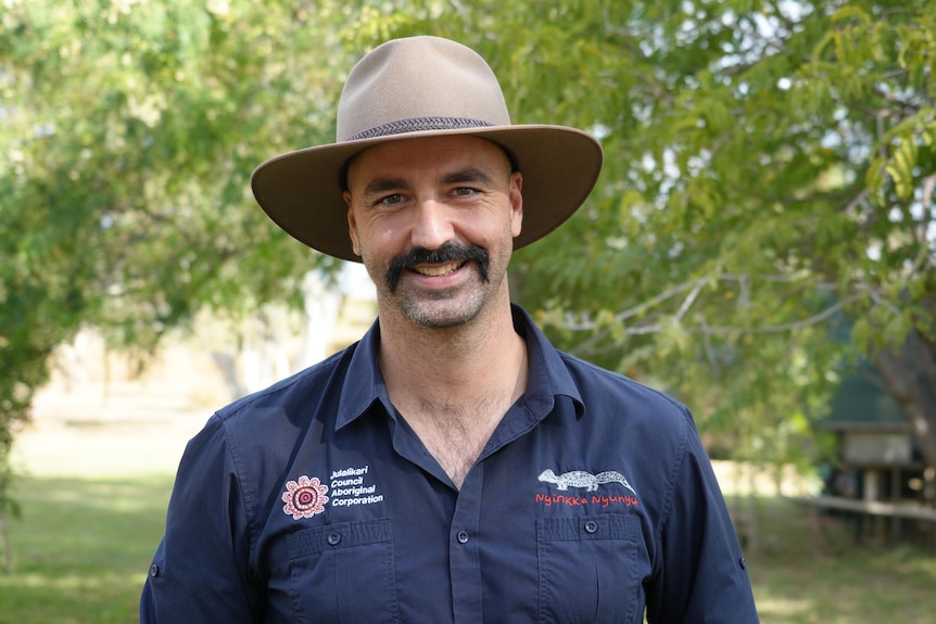 A mid shot of Lachlan wearing a navy Julalikari collared shirt and an akubra. Lachlan has a moustache.