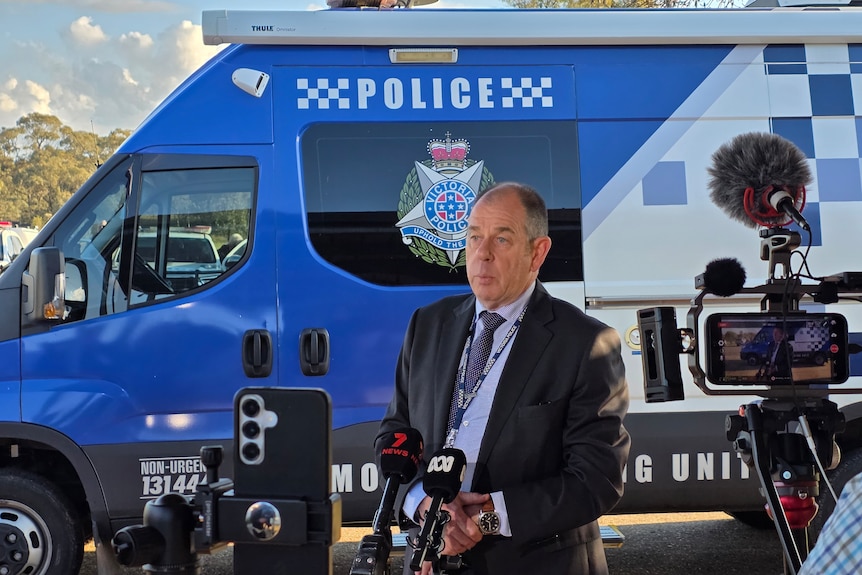 A police detective giving a press conference in front of a van