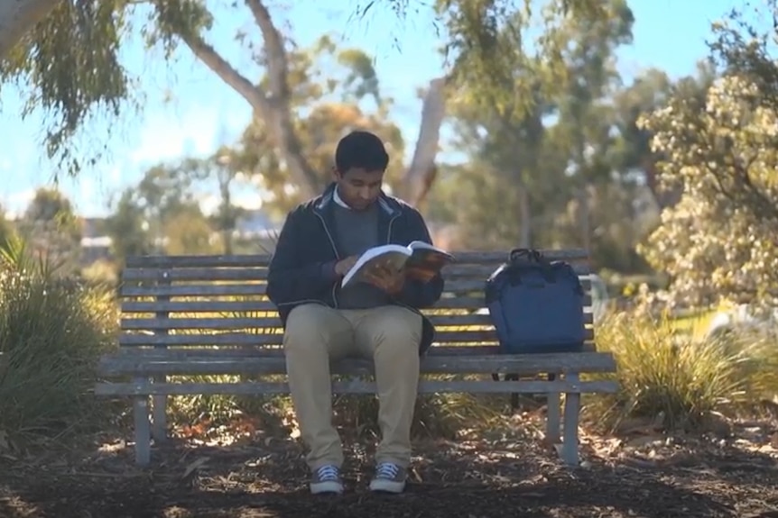 Man sits outside on a park bench reading a legal textbook.