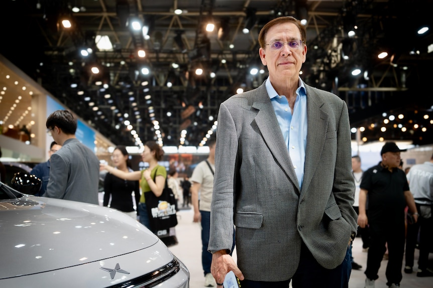 A man in a grey blazer and blue shirt, wearing glasses