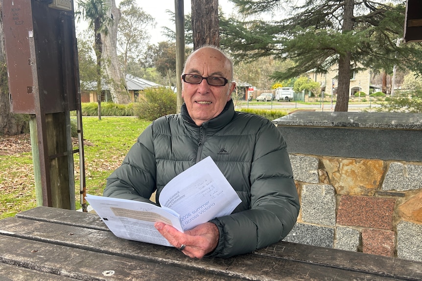 A man with glasses sits at a table and reads a report.
