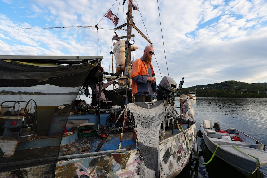 A man in a high-vis orange jacket standing on a boat.
