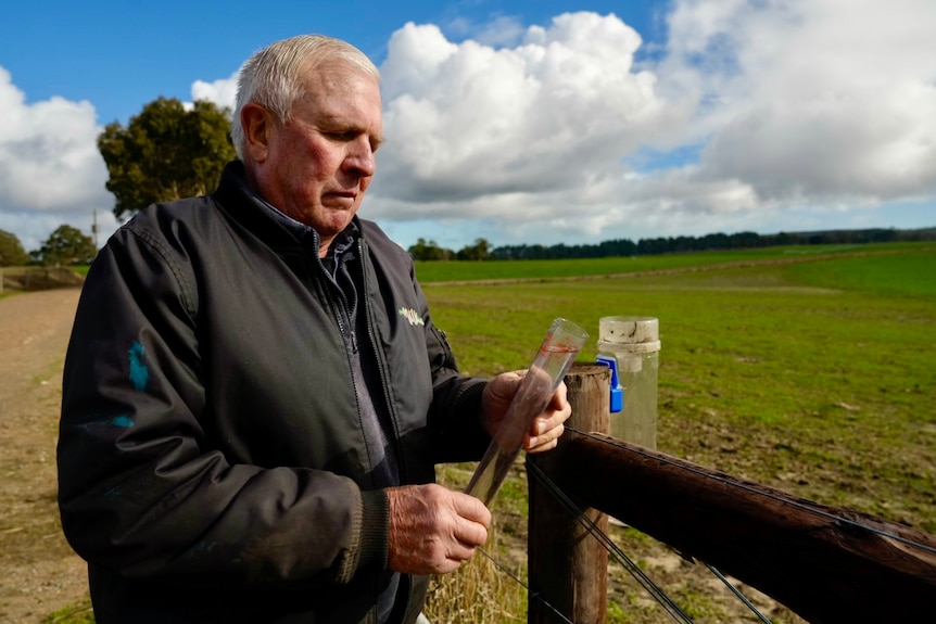 A nab wearing a puffer jacket stands in a paddock reading a rain gauge.