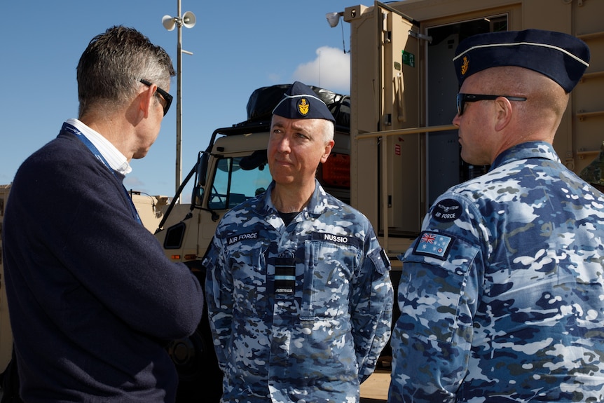 a man in an air force unifrom talks to a man in a suit in front of an army truck