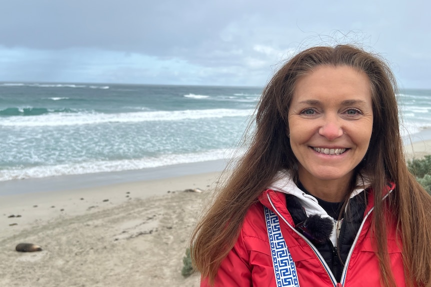 A woman with shoulder length brown hair in a pink wind jacket standing on a boardwalk