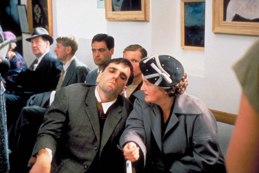 A woman sits closely by a man, both wearing grey.