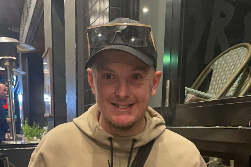 A man in a cap and hoodie sits in a beer garden.