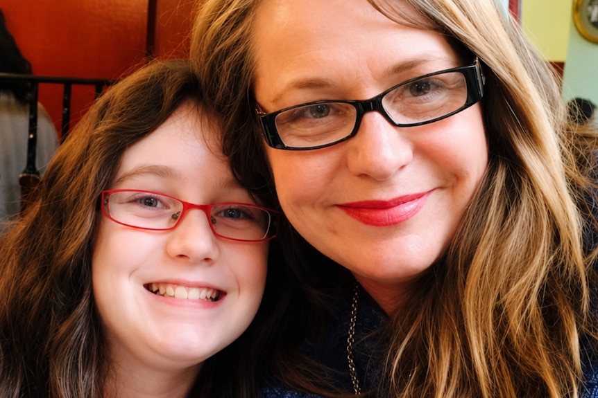 Woman in black glasses smiles closely to young girl in pink glasses