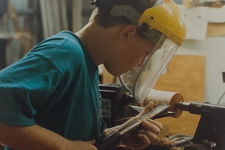 A young boy in a blue shirt doing woodwork.