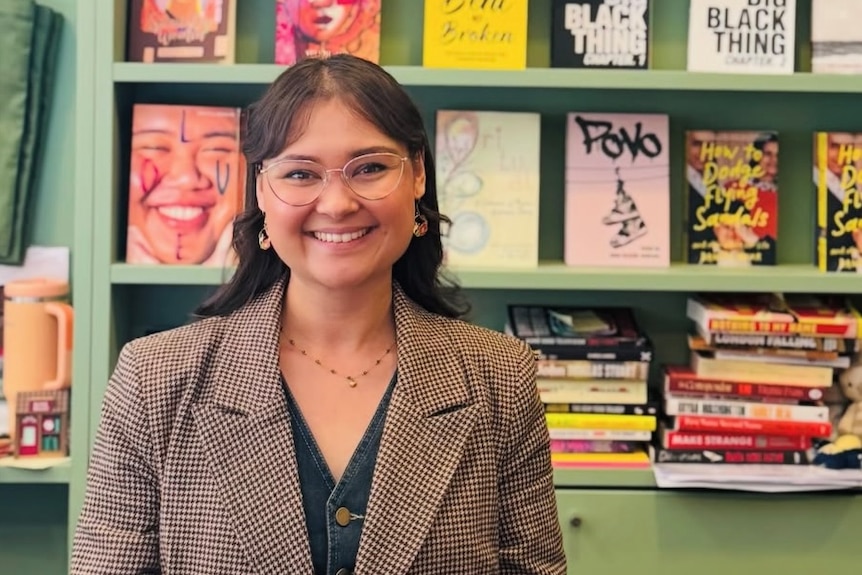 Mischa Parkee standing in front of a bookshelf, smiling, reading glasses, suit jacket