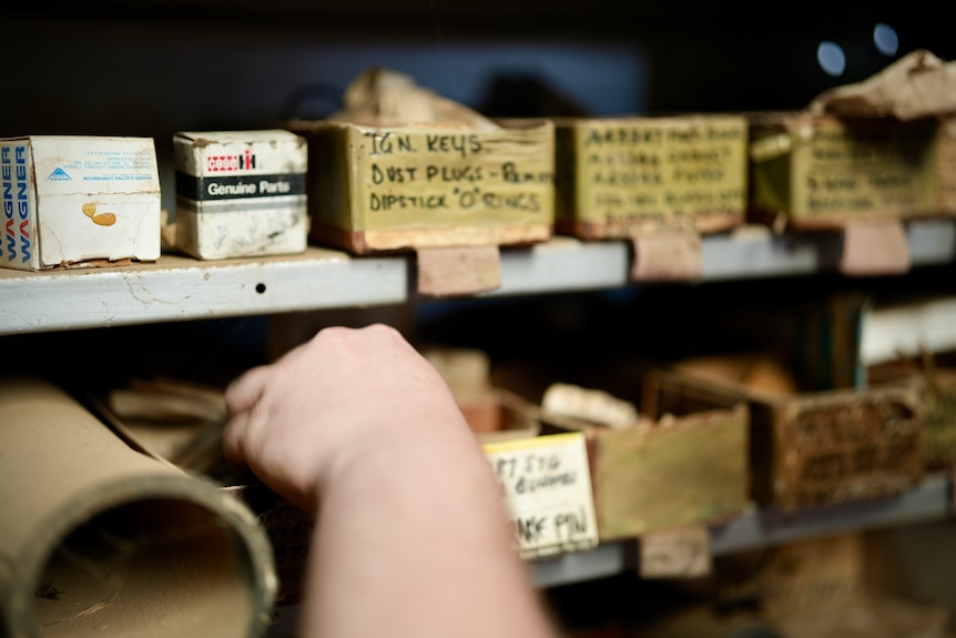 Close up of fingres reaching for small containers on the mechanic workshop shelves