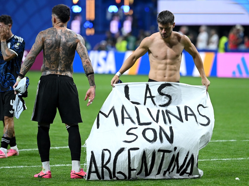 Two soccer players hold up a banner to the crowd.