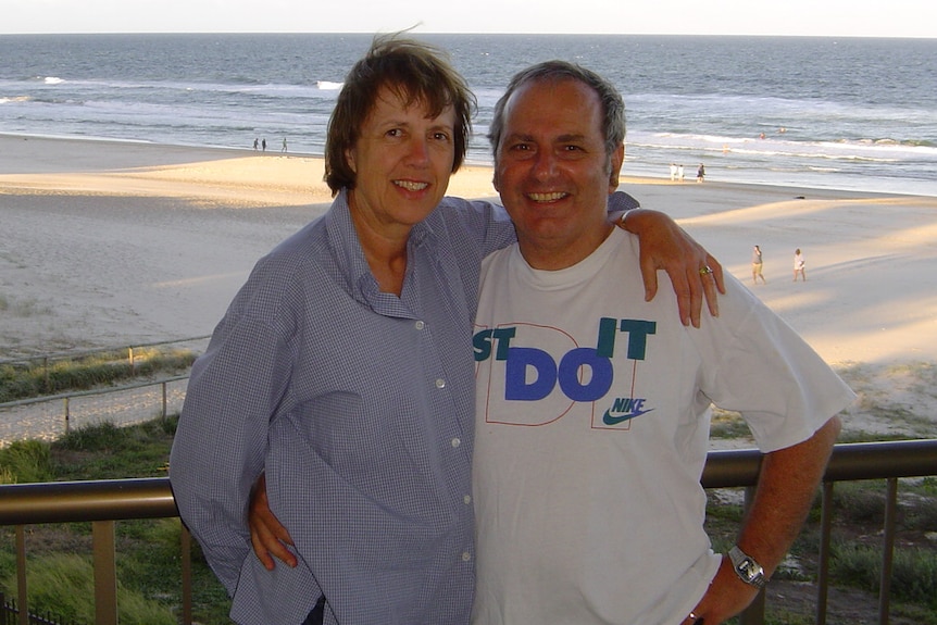 A smiling couple on a balcony which overlooks the beach.