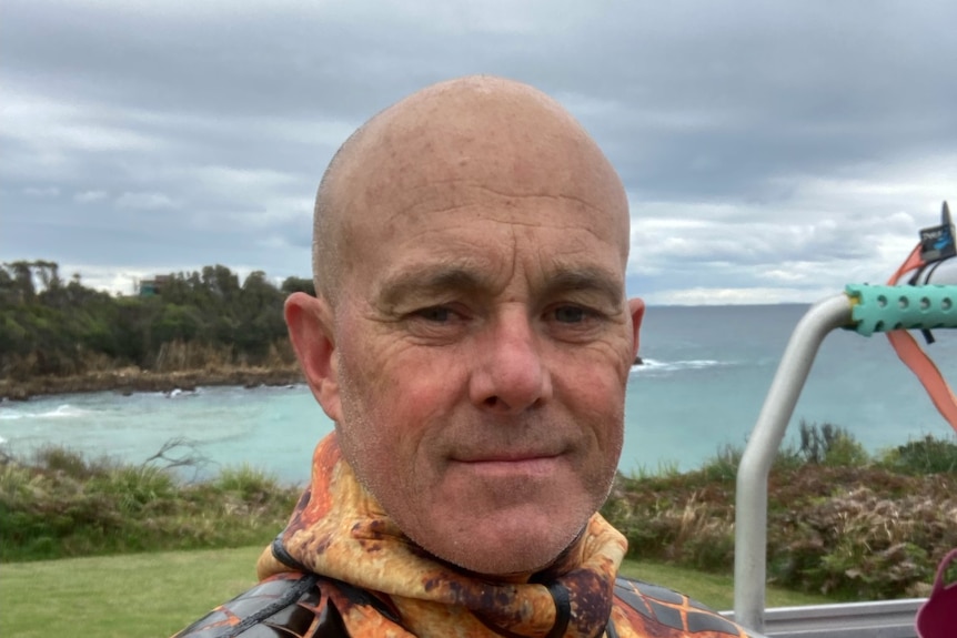 A bald man in a wetsuit looks towards the camera