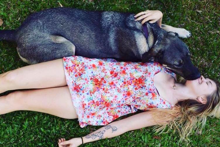 Toyah Cordingley lies on the grass smiling as she hugs her dog, date unknown.