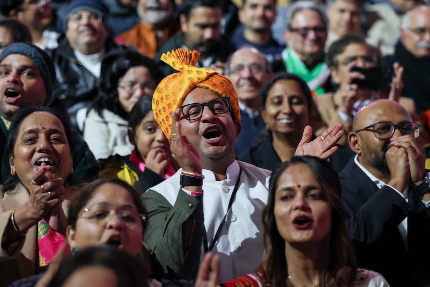 A crowd of people clap their hands and appear to be shouting.