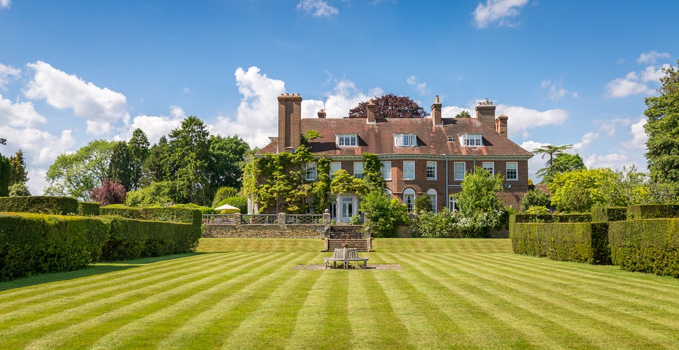 large brick house with manicured lawn and hedges under a blue sky.