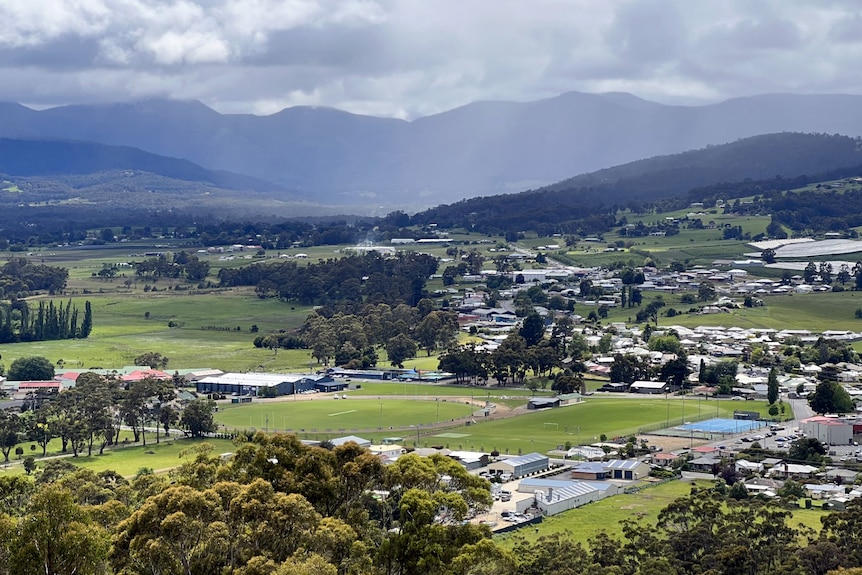 A view of a town and buildings in a green valley surrounded by mountains.