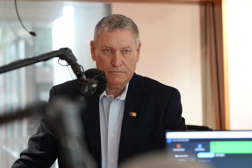 A man in a shirt and jacket behind a microphone