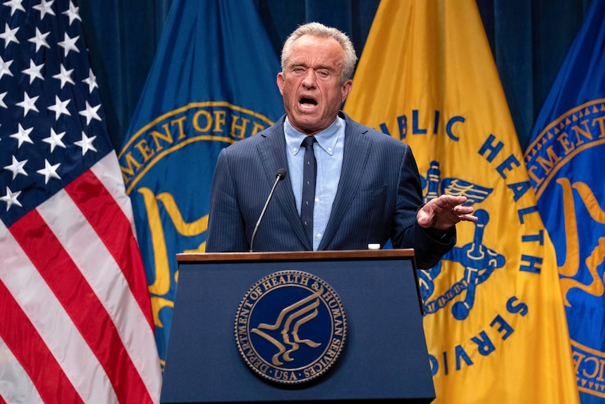 Robert F Kennedy Jr speaks from behind a lectern while wearing a navy blue suit