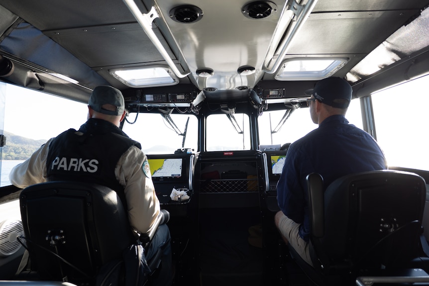 The backs of two people sitting down looking out a windscreen inside a boat