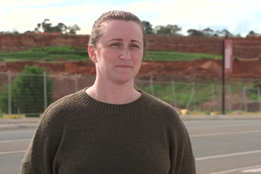 A woman stands across the road from a land redevelopment.