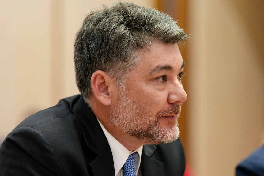 Close-up of a man in a dark suit being interviewed
