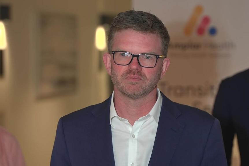 Chris picton in a dimly lit room in front of Peter Malinauskas and a banner