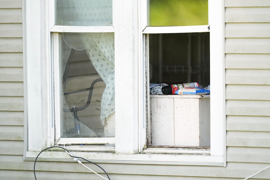 A close up of an open house window with partially drawn curtains and a bag of rice and insect killer sitting on a shelf