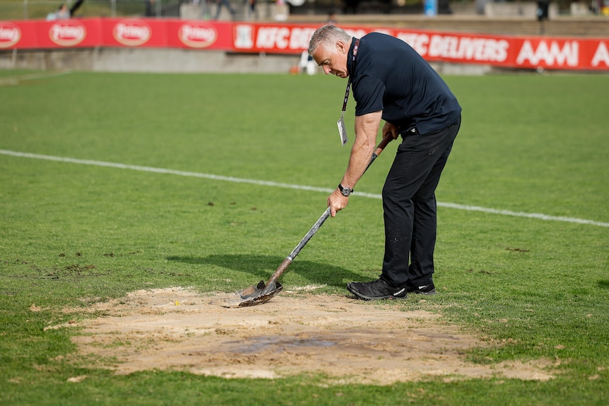 Sand is used to cover a hole in the ground due to a leak in an underground water pipe during an AFLW match.