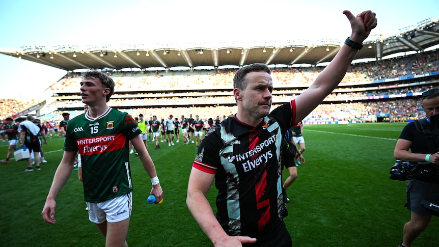 A Mayo team manager raises a thumbs up to the crowd as he and a player walk off after a big Gaelic games win.