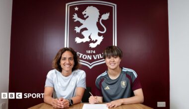 Akane Okuma signs contract in front of large Aston Villa emblem