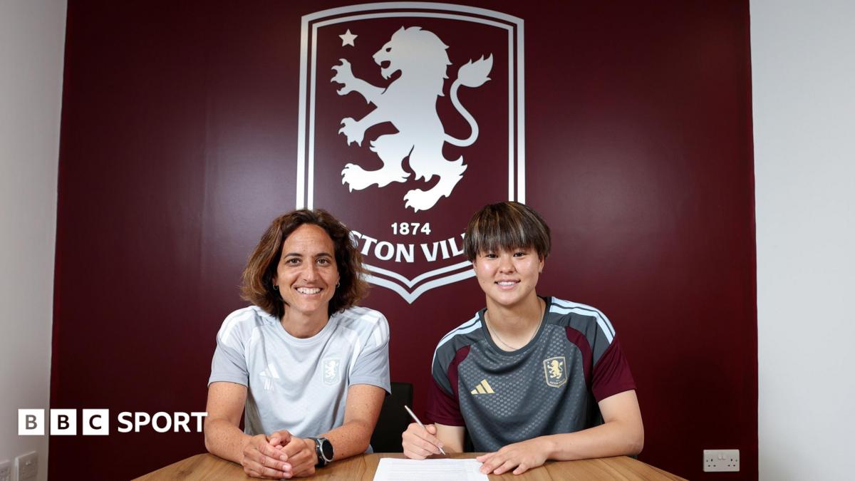Akane Okuma signs contract in front of large Aston Villa emblem