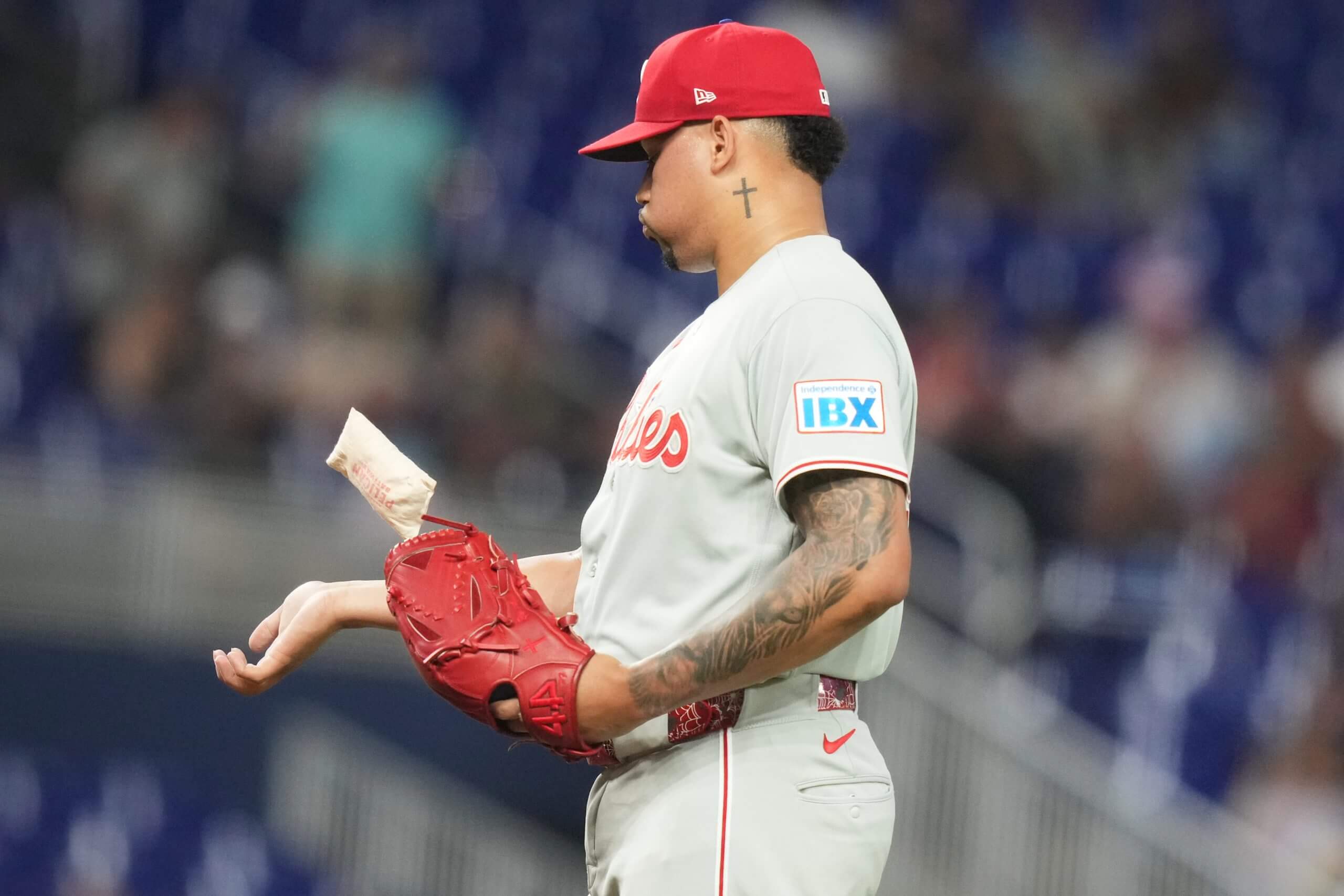 Jhoan Duran holds his glove in his left hand and extends his right arm in front of him, looking down at it. 