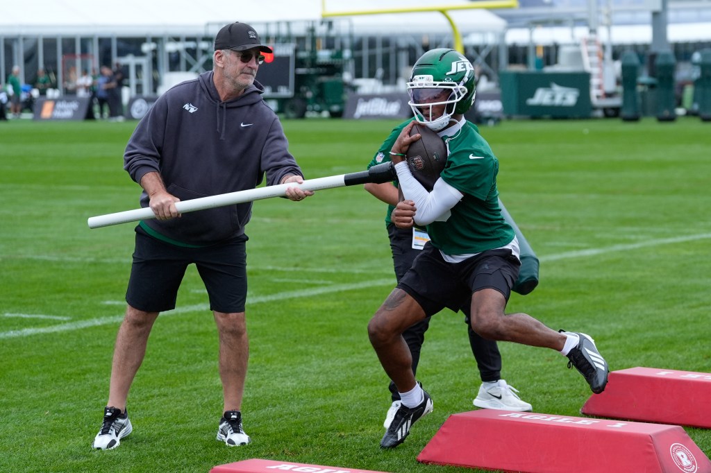 Frank Reich holds a long white pole that Garrett Wilson, in a green helmet and jersey, holds to his stomach with a football.