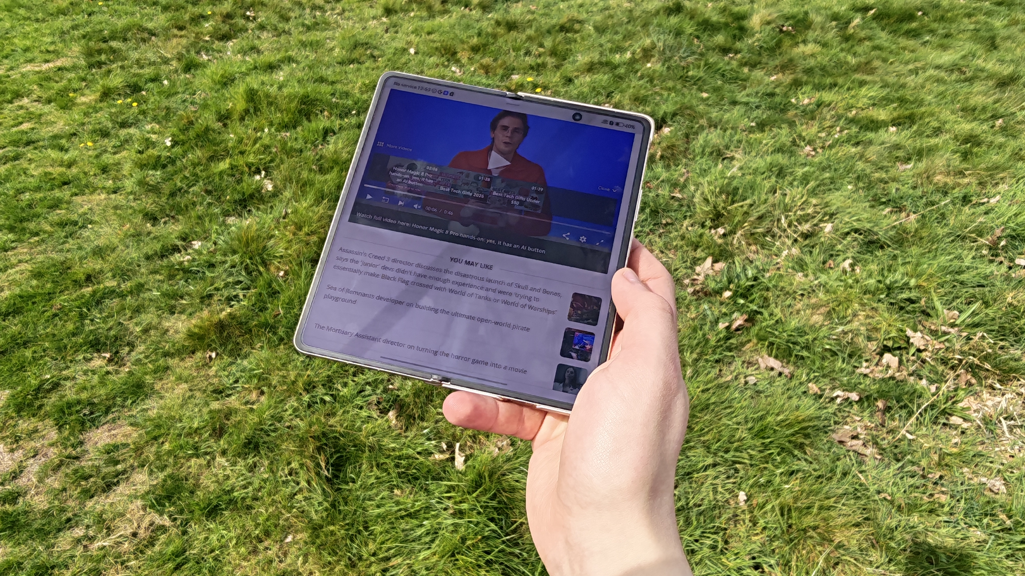 The Honor Magic V6 being held in a sunny field.