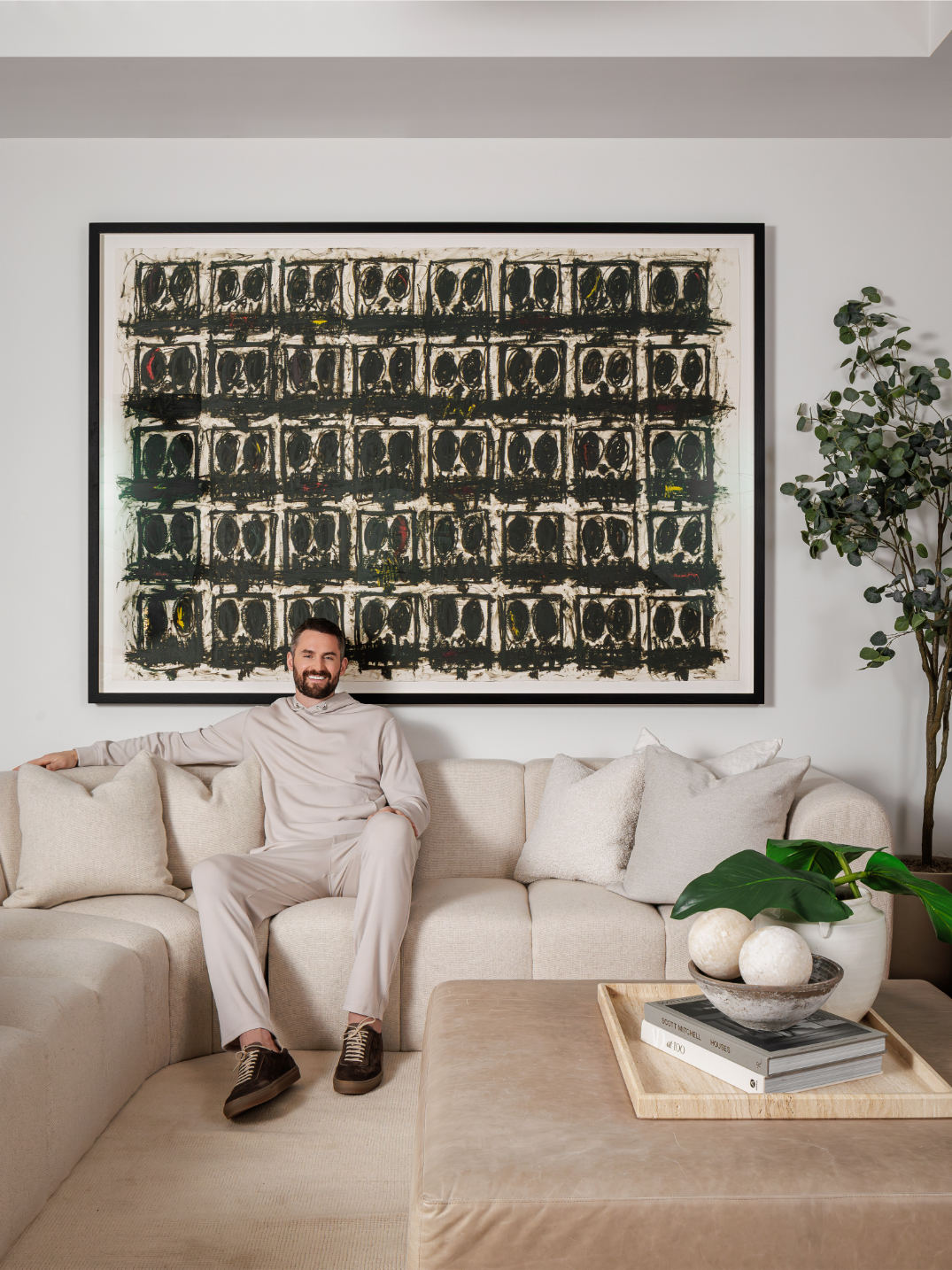 Kevin Love sitting on the couch in front of black Raashid Johnson painting