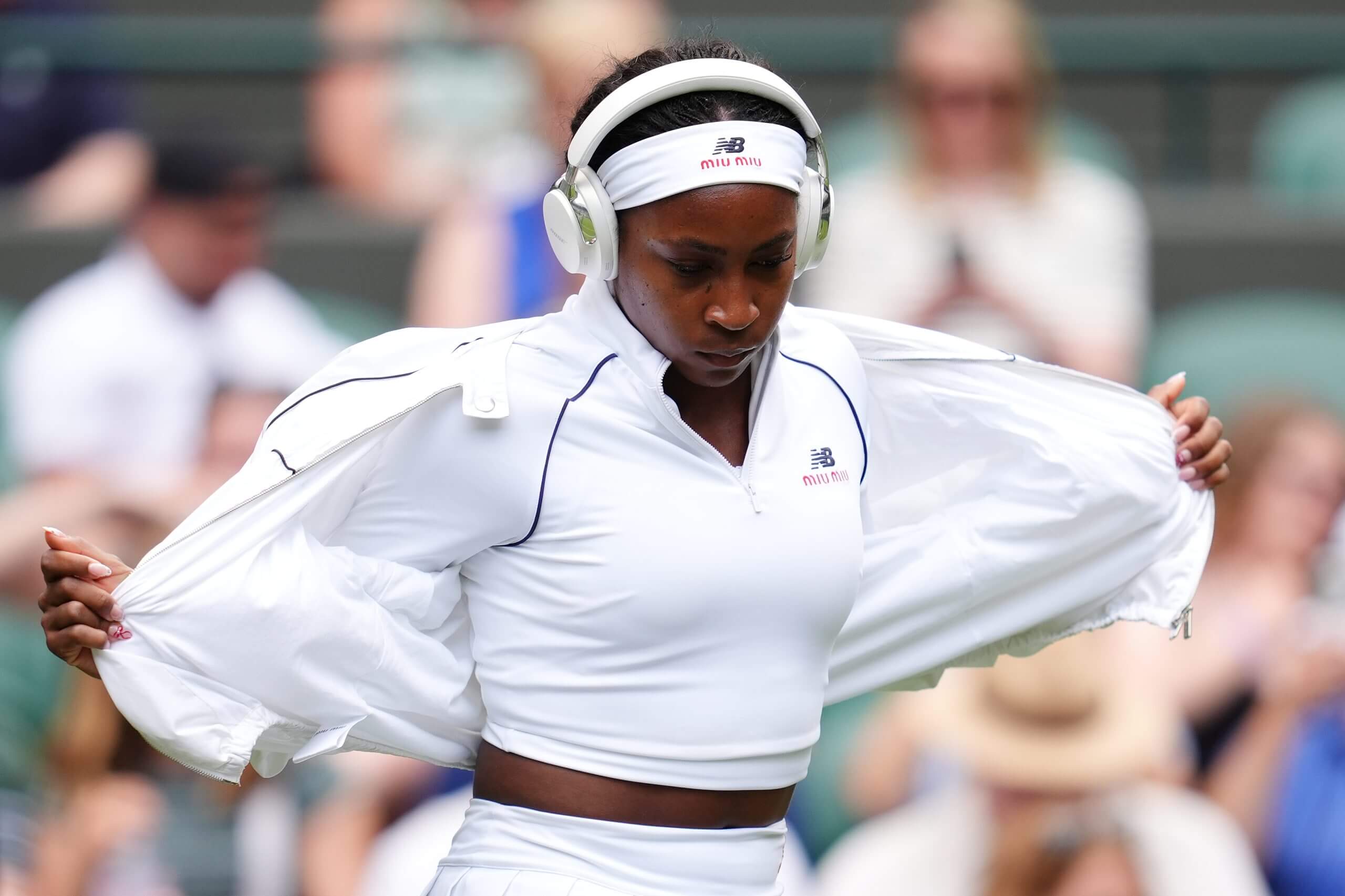 Coco Gauff wears a white two-piece outfit with trim details and New Balance and Miu Miu logos.