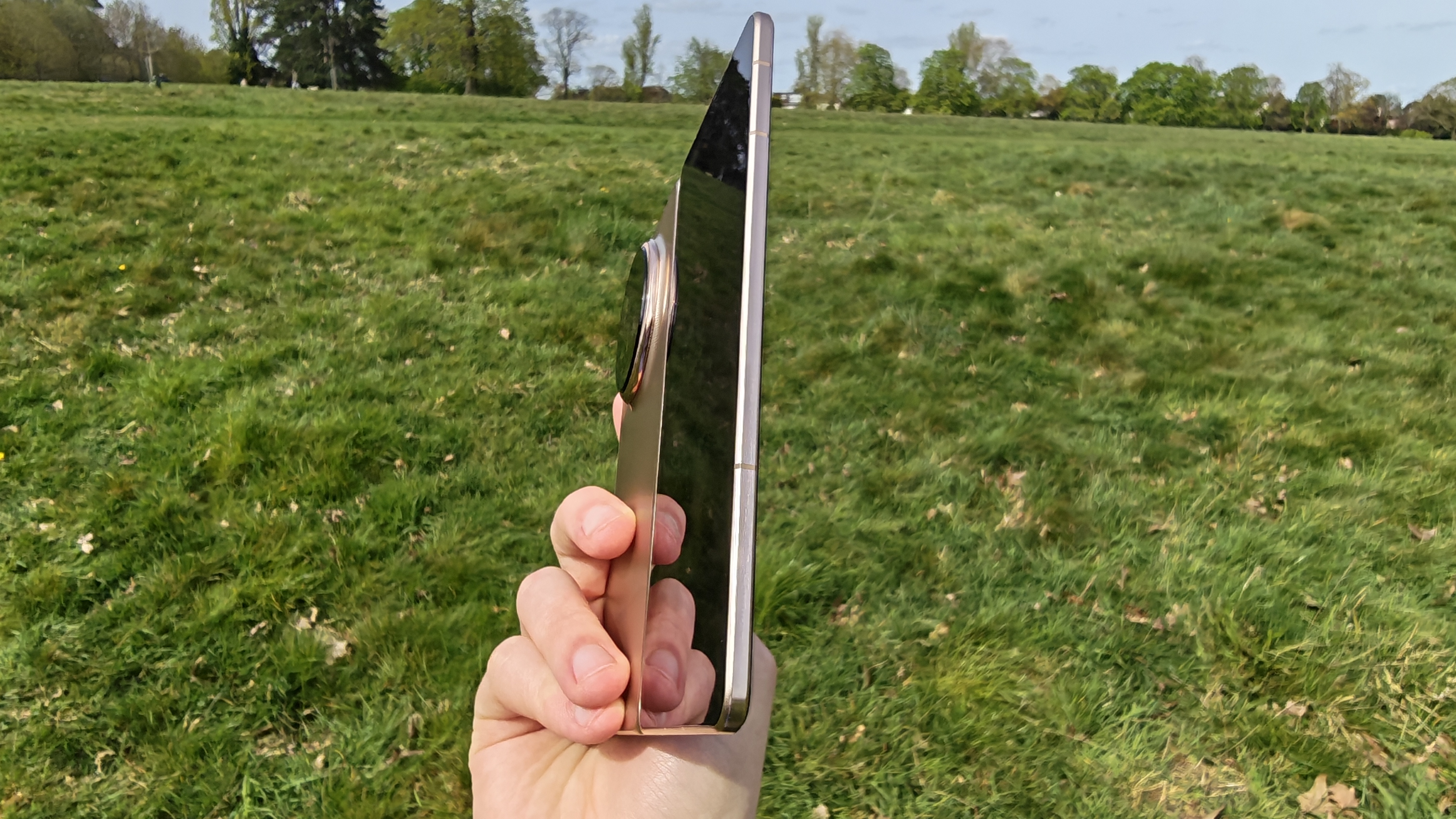 The Honor Magic V6 being held in a sunny field.