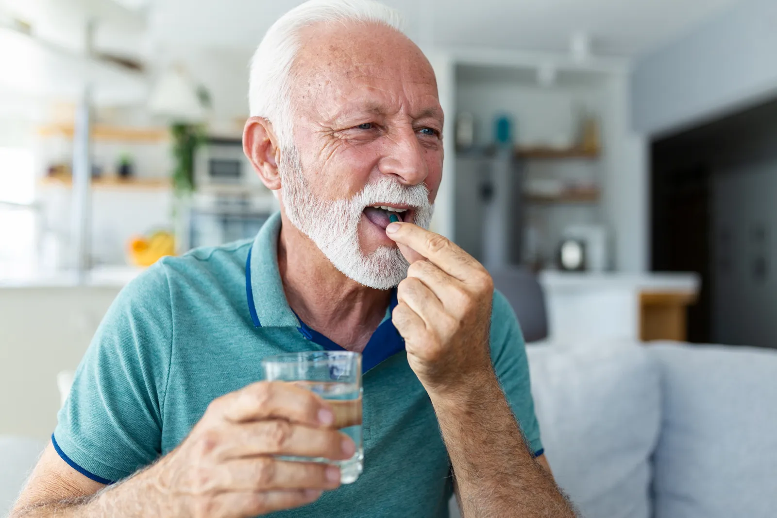 A stock image of a senior man taking a pill with glass of water in hand.