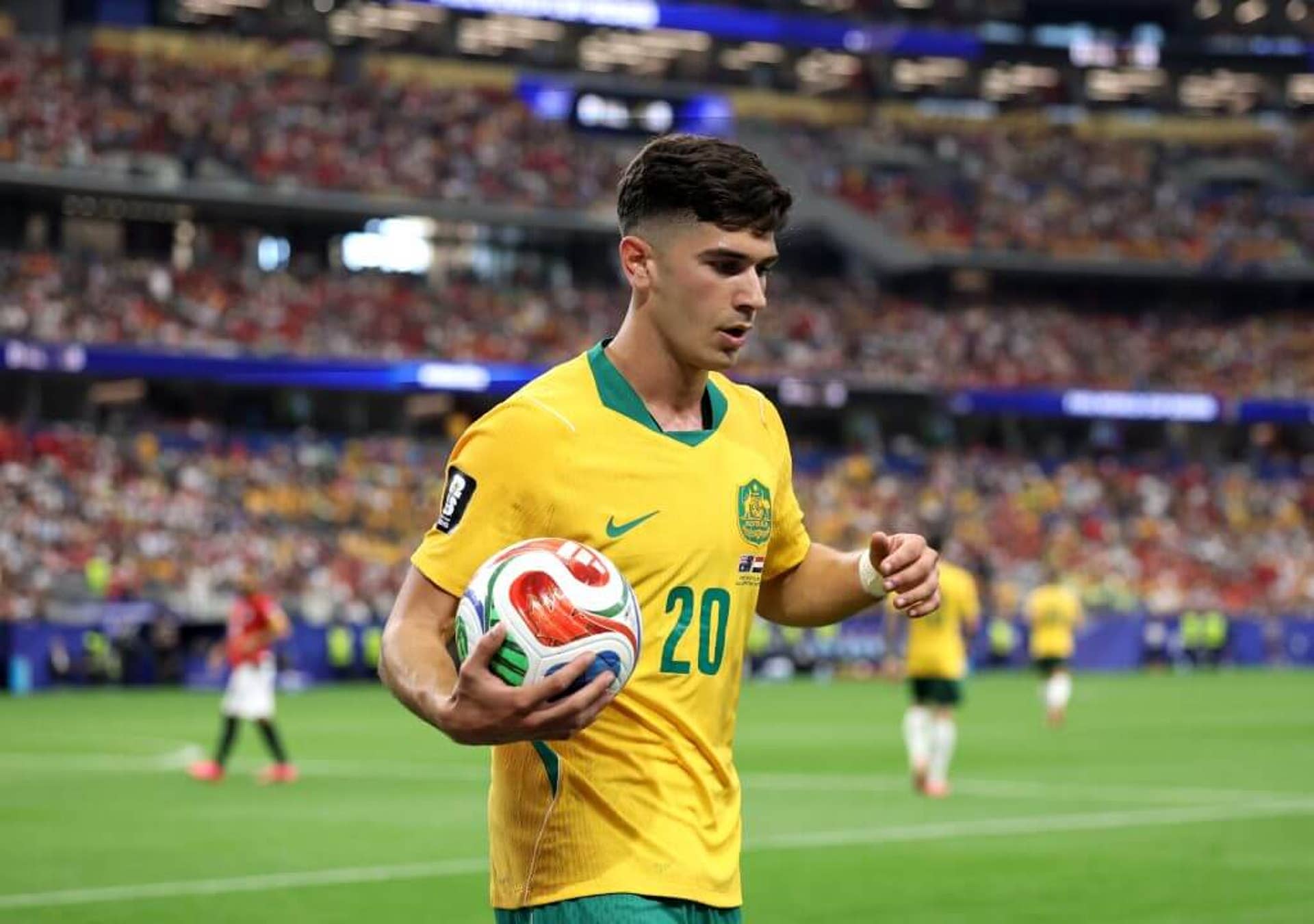 Cristian Volpato, wearing Australia's yellow home shirt, carries the ball in his right arm towards the corner flag
