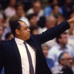 Walt Hazzard coaches from the sidelines Walt Hazzard, wearing a dark suit and patterned tie, points upward while coaching from the sidelines.
