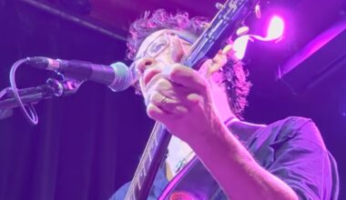 Jason Newsted playing an acoustic guitar onstage in 2026