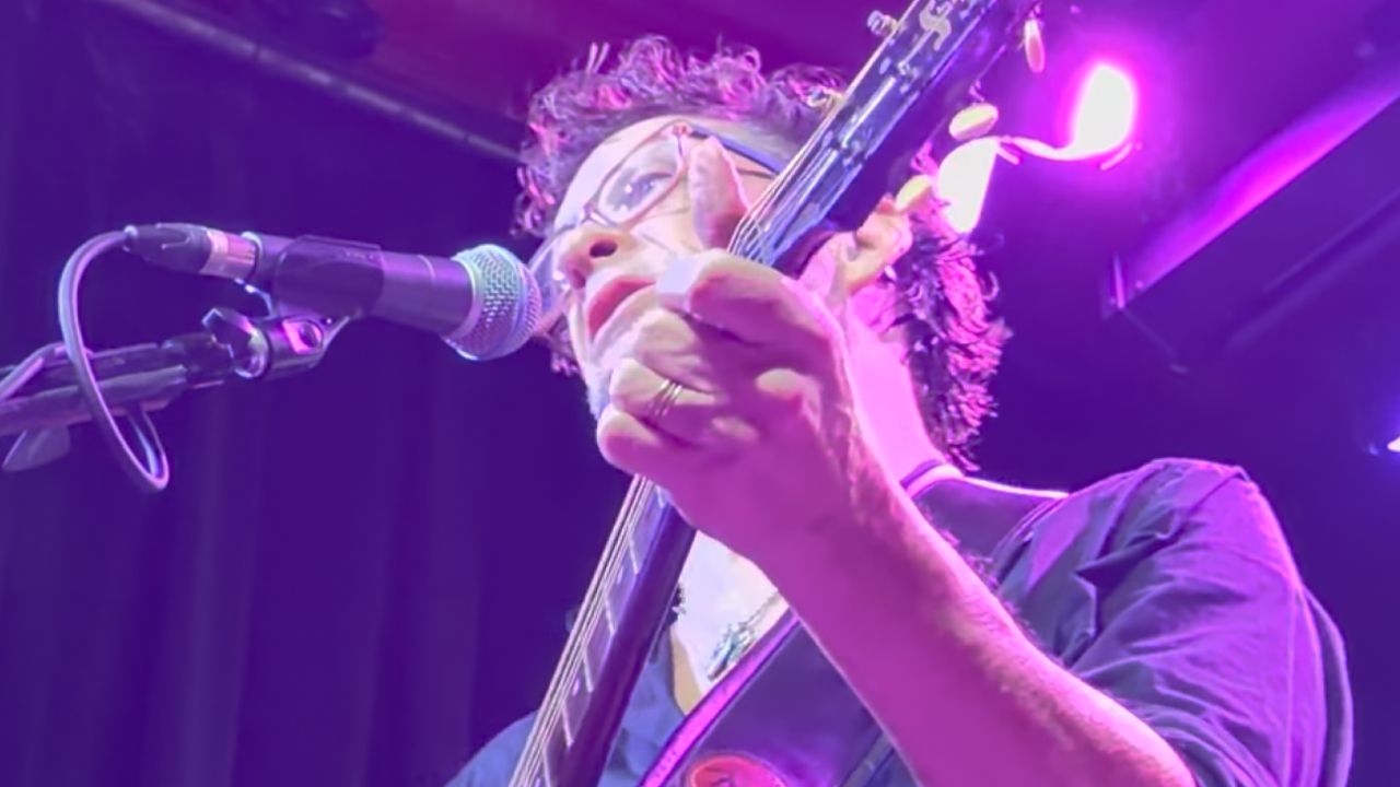 Jason Newsted playing an acoustic guitar onstage in 2026