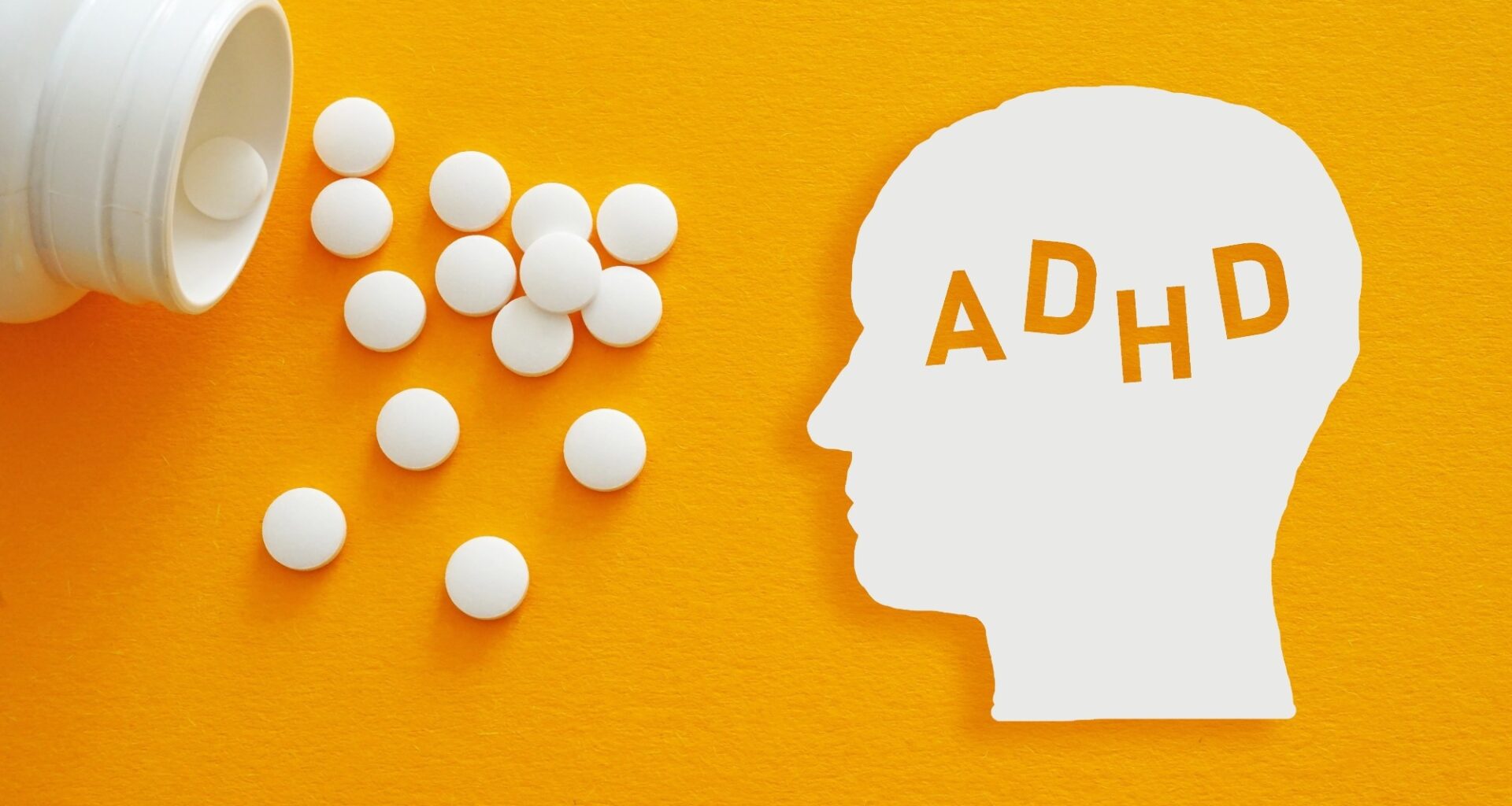 White ADHD head silhouette beside scattered medication tablets on a yellow background, illustrating stimulant treatment for attention deficit hyperactivity disorder.
