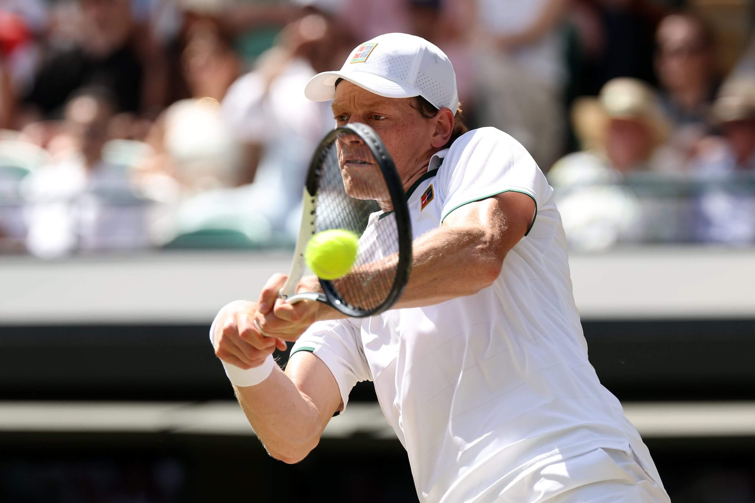 Jannik Sinner hits a two-handed backhand wearing an all-white tennis outfit.