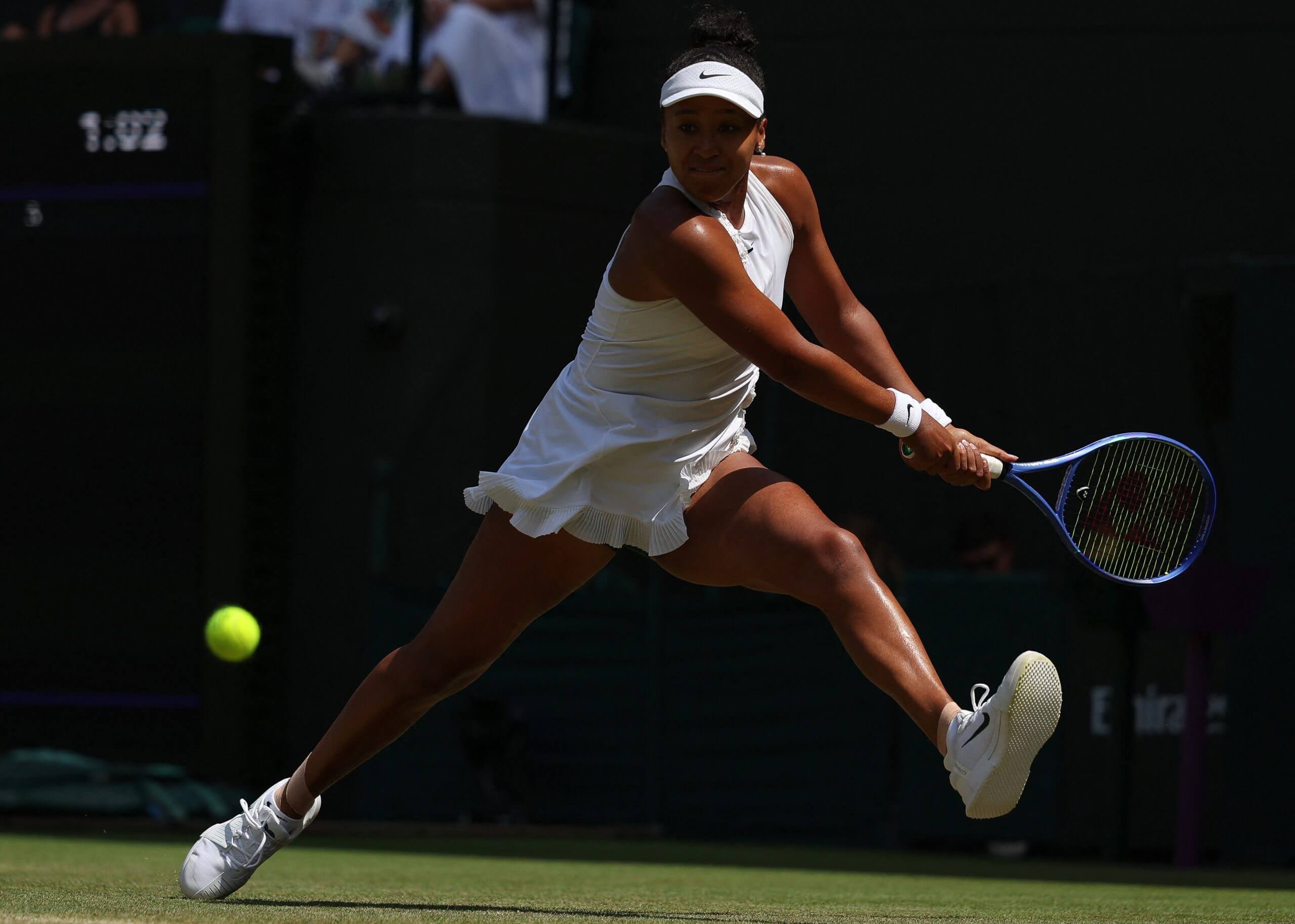 Naomi Osaka moves sideways to her left on a grass tennis court as a ball bounces into her strike zone.