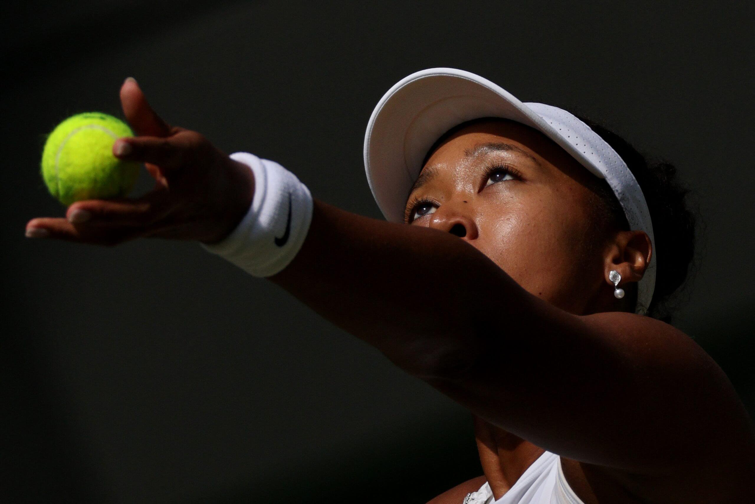 Naomi Osaka tosses a tennis ball into the air.