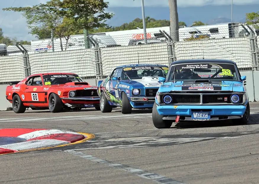 Three Touring Car Masters cars, a blue Ford Falcon, a Holden HQ Monaro and a red Ford Mustang, run nose to tail on the Townsville street circuit.